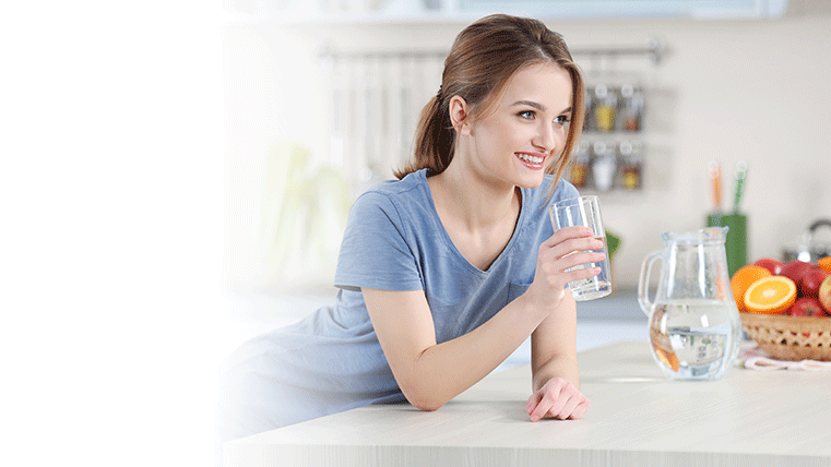 Mujer sonriente bebiendo agua sobre la encimera de una cocina.