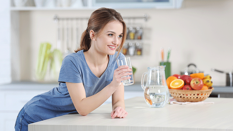 Mujer sonriente bebiendo agua sobre la encimera de una cocina.